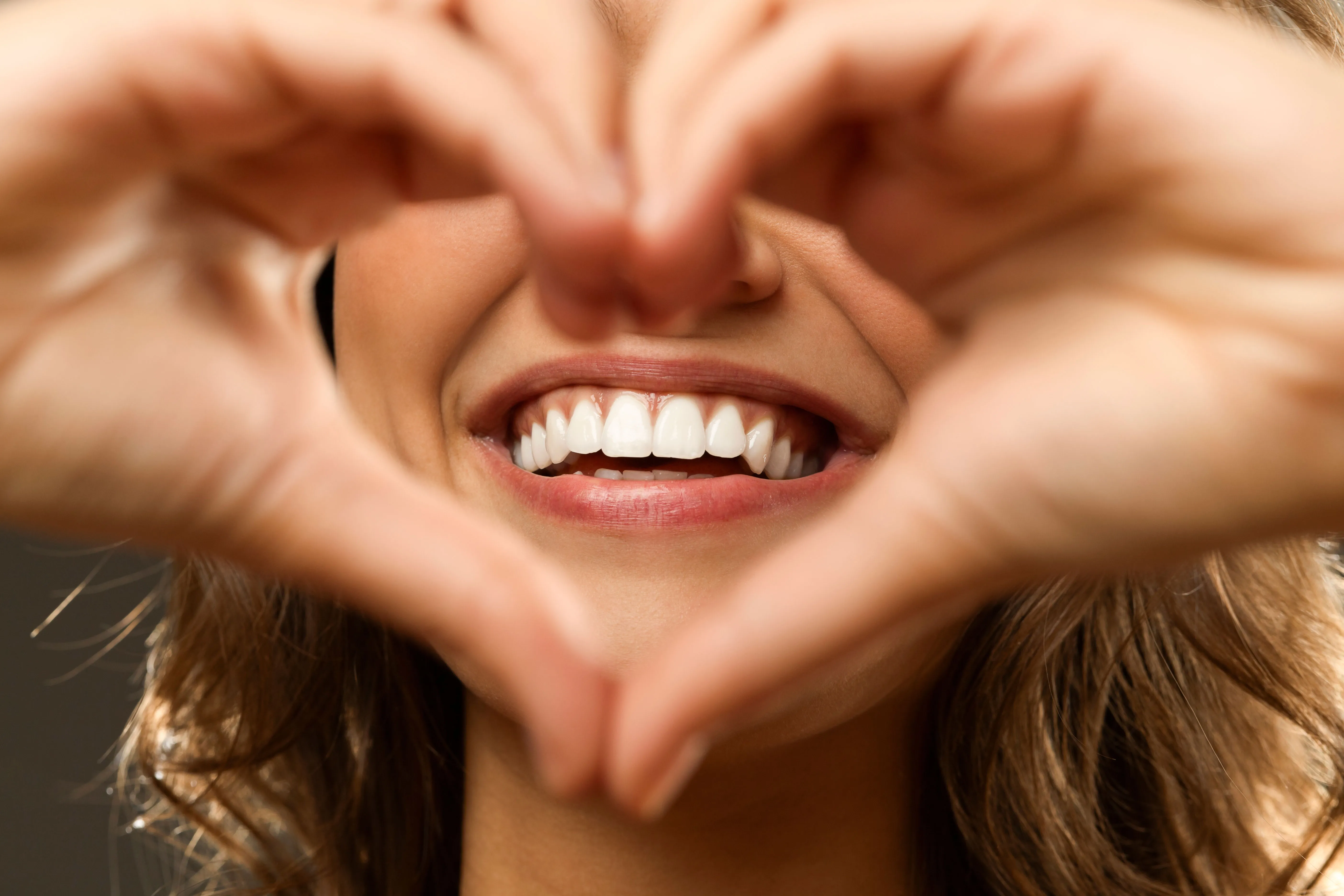 A woman framing her bright smile with her hands in a heart shape